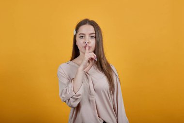 Pastel tişörtlü sakin bir kadın. Parmağını ağzının üstünde tutuyor. Sessizlik.