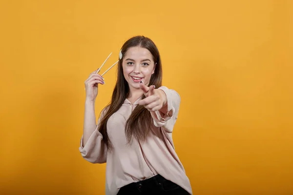 Mujer joven feliz sonriendo, señalando con el dedo a la cámara, manteniendo palos para el sushi — Foto de Stock