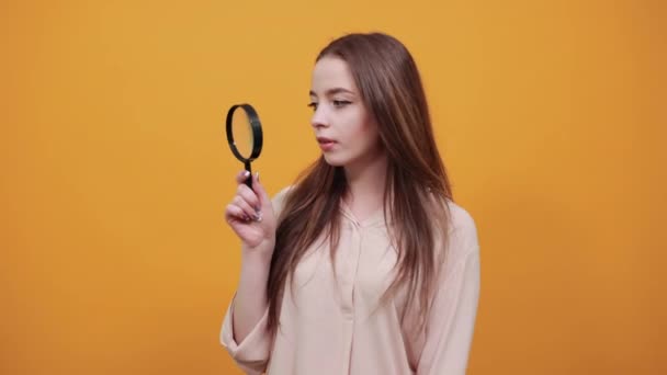 Cheerful woman in fashion pastel shirt keeping magnifier glass, looking on it — Stockvideo