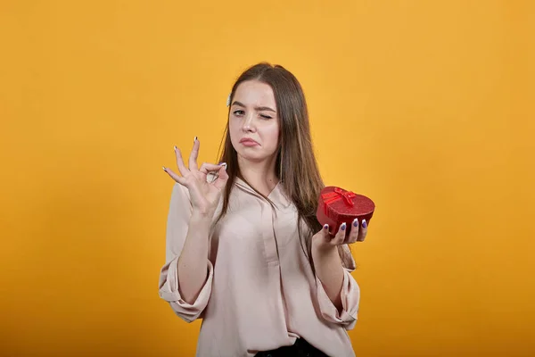 Atractiva mujer joven caucásica manteniendo la caja roja, haciendo buen gesto, guiños — Foto de Stock