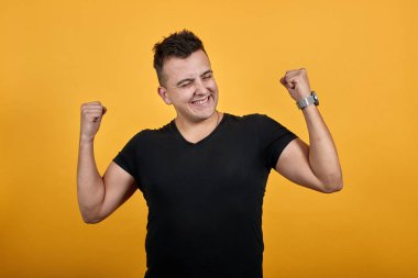 Charming young man doing winner gesture, smiling, keeping fists up.