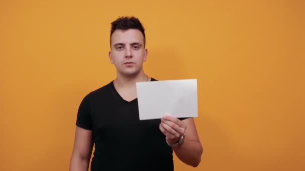 Snygg kaukasisk ung man som håller vitt tomt, visar tummen framför kameran. — Stockvideo