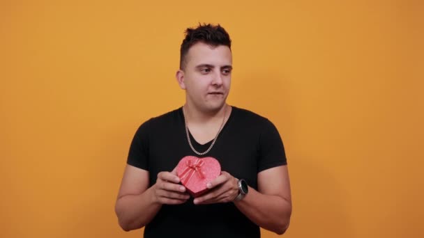 Красивый кавказский молодой человек держит красную коробку, машет кулаками, улыбается . — стоковое видео