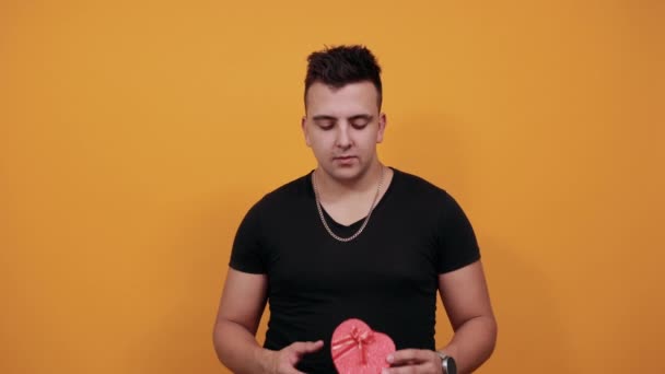 Удивленный молодой человек держит розовую коробку, грызет ногти . — стоковое видео