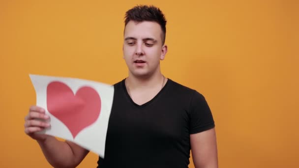 Unhappy man keeping picture of heart, holding gun with fingers near head. — Stock Video