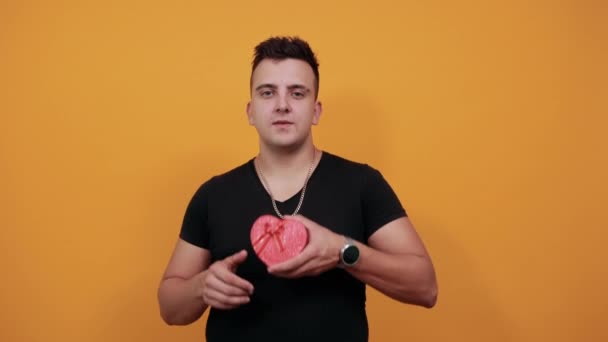 Handsome young man smiling, covered face with palm, keeping red box. — Stock Video