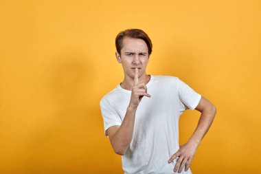 Beyaz t-kısa giyen erkek sessizlik işareti olarak işaret parmağını ağzına tutar..