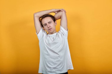 Beyaz tişörtlü adam sarı arka planda elini kaldırdı.