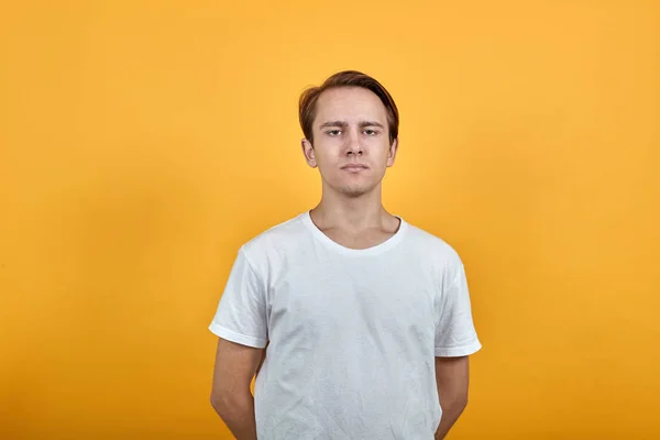 Ung man i vit t-shirt på gul bakgrund har händerna bakom ryggen — Stockfoto