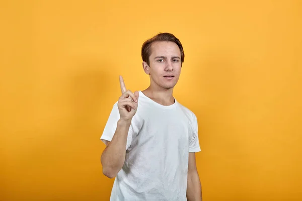 Ung man i vit t-shirt höjer pekfingret i ett tecken på ny idé. — Stockfoto