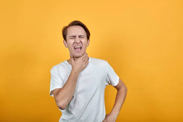 Человек с больным горлом, держащийся за шею на желтом фоне — стоковое фото