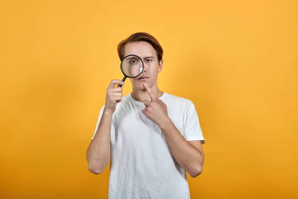 A young man shows his pimple or blackhead through a magnifying glass. — Stock Photo, Image