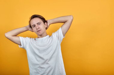 Beyaz tişörtlü genç adam ellerini sarı arka plana koyar..