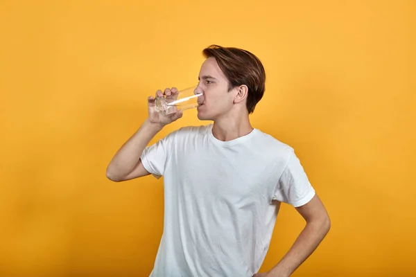 Homme en t-shirt blanc boit l'eau d'un verre sur fond jaune . — Photo