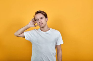 Beyaz tişörtlü bir adam sarı arka plandaki dedikoduları dinliyor.