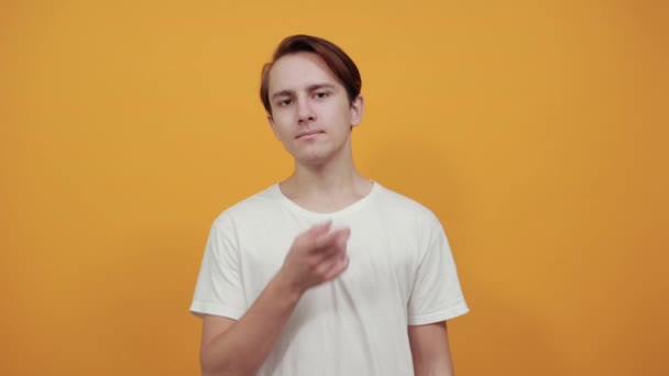 White t-shirt yellow background brunette man shows fingers on acne on his face — 비디오