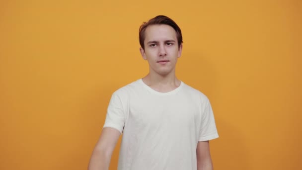 Młody mężczyzna w białej koszulce pokazuje palcem wskazującym, że dobrze sobie radzi — Wideo stockowe