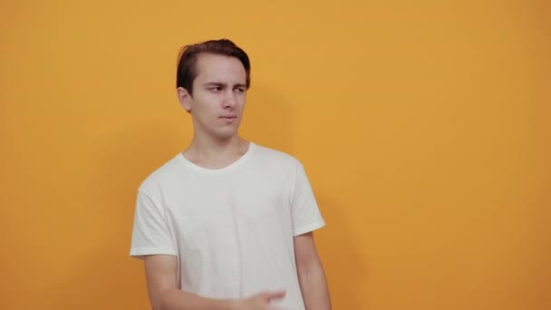 Homem com t-shirt branca surpreendido mostra a direção do dedo ou aponta para objeto — Vídeo de Stock