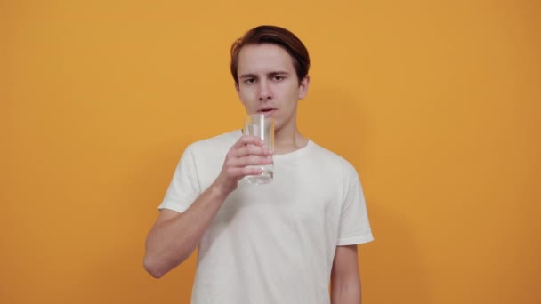 Чоловік п'є воду зі склянки, на жовтому тлі білої футболки . — стокове відео