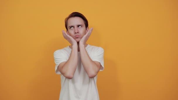 Jongeman in wit t-shirt kantelt zijn hoofd en ondersteunt zijn kin met zijn handen — Stockvideo