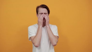Beyaz tişörtlü, sarı arka planda ağlayan üzgün adam elleriyle işaret ediyor..