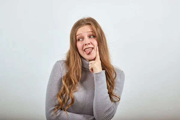 Een meisje van europese verschijning toont tong grijs achtergrond. — Stockfoto