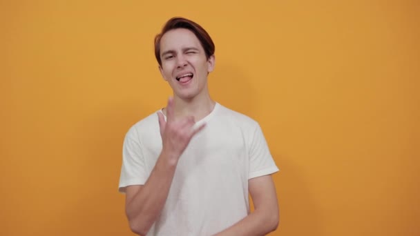 Чоловік у білій футболці показує рок-стиль і розтягує язик — стокове відео