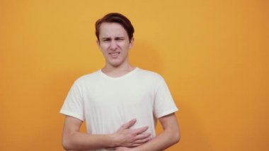 Mide ağrısı, beyaz tişört, sarı arka planda genç erkek..