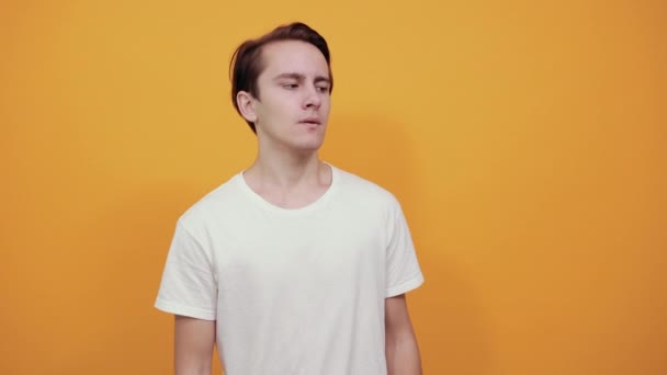 Man i vit t-shirt på gul bakgrund ser tryggt åt sidan håller händerna — Stockvideo