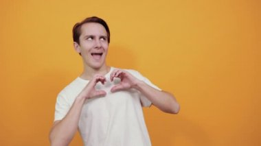 Beyaz tişörtlü genç bir adam elleriyle kalbi şekillendirdi ve başka yere baktı.