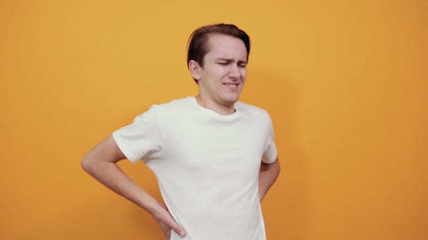 Young man with back pain holding her lower back on yellow background. — Stock Video