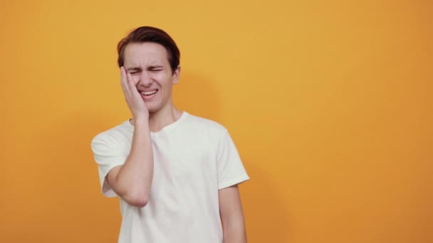 Ein Mann im weißen T-Shirt berührt sein Gesicht mit der Hand und lacht in die Kamera. — Stockvideo