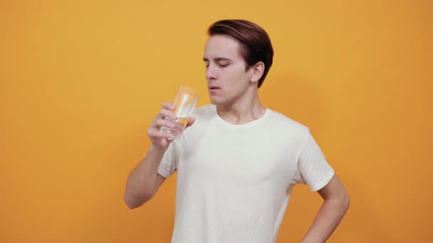 Man in een wit t-shirt drinkt water uit een glas op gele achtergrond. — Stockvideo