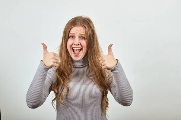 En ung kvinna i grå tröja med rött hår ser glad ut och ger två tummar upp — Stockfoto