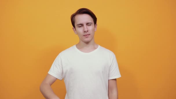 Un joven en camiseta blanca con expresión divertida en la cara muestra su lengua — Vídeo de stock