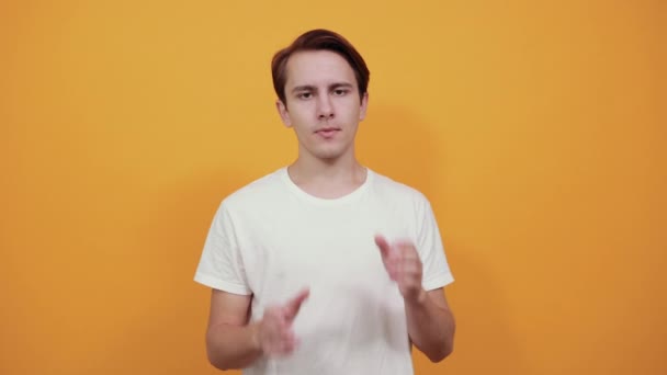 Молодий чоловік у білій футболці, який тримає голову руками, дивиться вперед — стокове відео