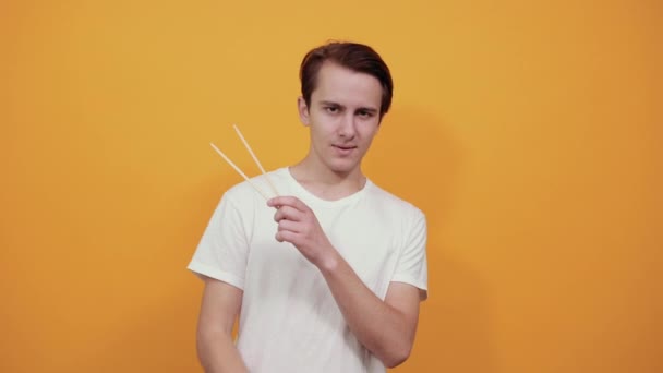 A young man in white t-shirt shows large index finger and Chinese chopsticks — 비디오