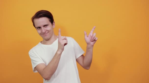 Un joven guapo señala la dirección con los dedos en camiseta blanca — Vídeos de Stock