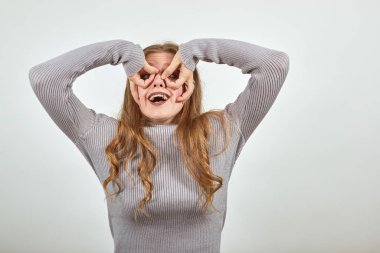 Gri kazaklı kızıl saçlı kadın ters dönmüş elleriyle taklit gözlük takıyor.