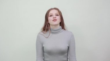 Gri kazaklı güzel kızıl saçlı kadın başını eğiyor ve mutlulukla gülümsüyor.