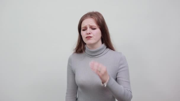 A young beautiful red-haired woman in a gray sweater shows headache migraine — 비디오