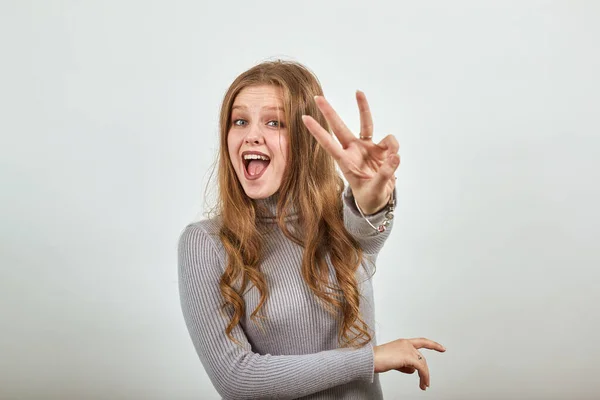 Hermosa mujer pelirroja en un suéter gris es feliz mostrando tres dedos —  Fotos de Stock