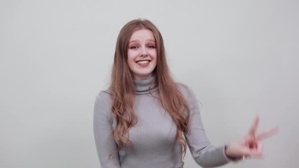 Жінка в сірому светрі щаслива з гарним настроєм посміхається і показує своїм пальцям два — стокове відео