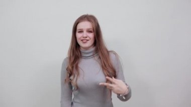 Gri kazaklı kadın mutlu, neşeli gülümseyen ve iki parmağını gösteren.