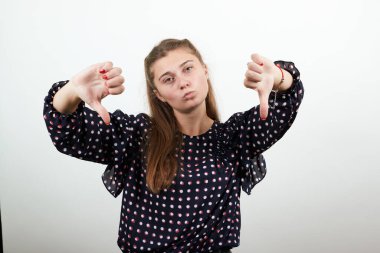 Beyaz halkalı siyah elbiseli kız kötü ruh haliyle baş parmağını indiriyor.