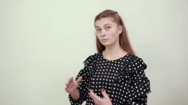 Beyaz halkalı bir elbise içindeki kız. Şaşırmış bir ifade. El hareketleriyle.