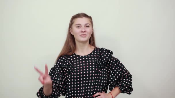 Girl in black dress with white circles shows off two fingers and smiles happily — 비디오