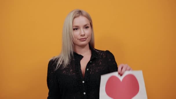 Mulher feliz segurando um pedaço de papel com um coração vermelho e um gesto de mão — Vídeo de Stock