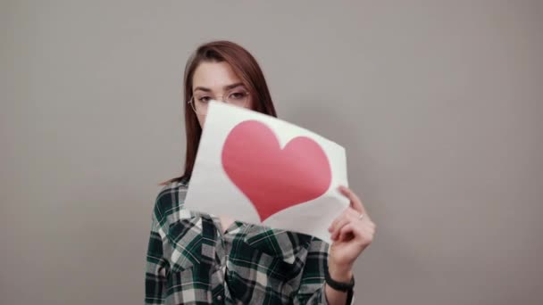 Unhappy woman with glasses holds piece of paper with red heart in hand — ストック動画