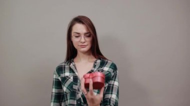 insulted woman holds gift red box in the form of heart, stops with palm of hand